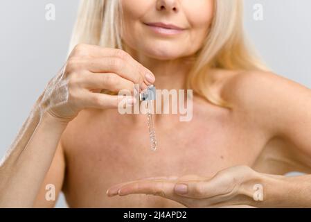Zugeschnittenes Bild einer Frau mittleren Alters, die Hautpflegemittel mit Tropfflappen verwendet, weibliche Hände, die eine Pipette mit Anti-Aging-Serum-Essenzen-Öl halten, Werbekonzept Stockfoto