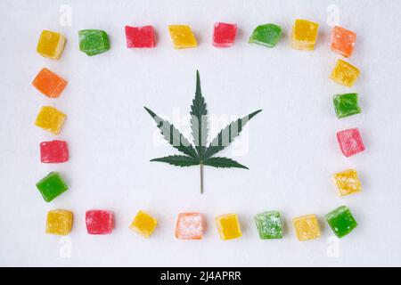 Layout von bunten Marmelade und Marihuana-Blatt auf weißem strukturiertem Hintergrund. Süßigkeiten mit CBD-Öl. Draufsicht, flach liegend. Stockfoto