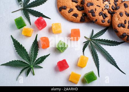 Marmelade und amerikanische Kekse mit Cannabisextrakt. Süßigkeiten mit CBD-Öl. Marihuana Blätter auf weißem Hintergrund. Draufsicht, flach liegend. Stockfoto