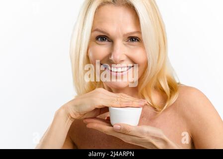Hautpflege-Routine. Charmante Mitte des Alters blonde 40s Frau hält Glas mit Anti-Aging-Feuchtigkeitscreme, Blick auf die Kamera isoliert auf weißem Hintergrund, kopieren Raum. Werbekonzept Stockfoto