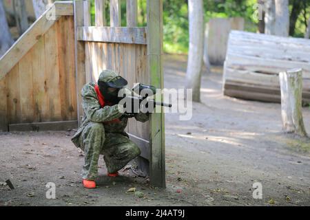 Paintball-Spieler in voller Ausrüstung schießt auf dem Schießstand Stockfoto