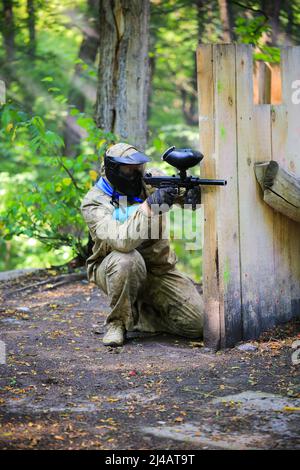 Paintball-Spieler in voller Ausrüstung schießt auf dem Schießstand Stockfoto