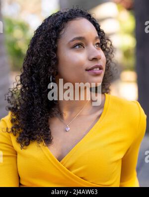 Nahaufnahmen von Porträts einer jungen schwarzen Frau im strahlenden Sonnenlicht, die in einem Garten sitzt Stockfoto