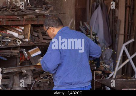 MARRAKESCH, MAROKKO - 21. NOVEMBER; 2018 Metallarbeiter in blauem Overall in der Medina Stockfoto