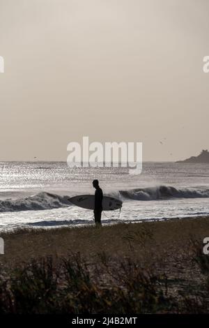 Silhouette eines Surfers mit Brett am Strand mit Chauveau Leuchtturm, dem berühmten Leuchtturm in der Nähe von La Rochelle und Re Insel Stockfoto