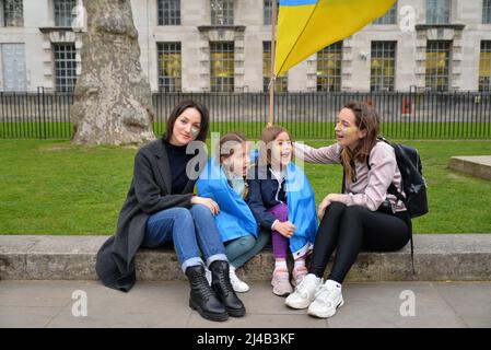 London, Großbritannien. 13. April 2022. In Whitehall gegenüber der Downing Street, die ukrainische Nationalhymne während eines Protestes gegen die russische Invasion in der Ukraine sang - links, Natalia und ihre Tochter Elizabeth (6) sitzen mit ihren Cousins - Olha und ihre Tochter Mira (6), die vor 2 Tagen als Flüchtlinge aus Kiew in Großbritannien angekommen sind. Kredit: Mark York/Alamy Live Nachrichten Stockfoto