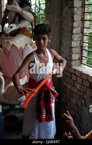 Munshiganj, Bangladesch. 13. April 2022. Ein Hindu-Anhänger sah, wie er ein Schwert färbt, um an der Lal-Kach-Prozession teilzunehmen. Das Lal Kach (Red Galss) Festival wird in der lokalen Gemeinde seit vielen Jahrzehnten gefeiert. Die Hindu-Männer malen sich rot an und nehmen an einer Prozession mit Schwertern Teil, während sie Macht gegen böse Sprites zeigen, während sie ein Jahr beenden und ein weiteres bangladesches Neujahr begrüßen. Kredit: SOPA Images Limited/Alamy Live Nachrichten Stockfoto