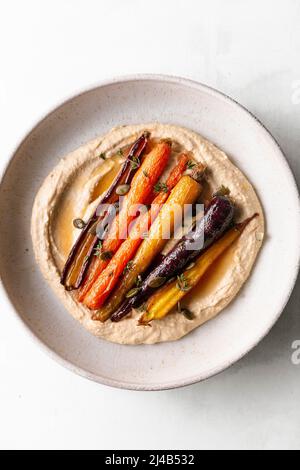 Honiggeröstete Karotten mit Hummus in einer Keramikschale. Stockfoto