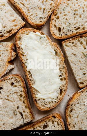 Gebutterte Scheibe Rosmarin-Sauerteig-Brot, umgeben von vielen Scheiben. Stockfoto