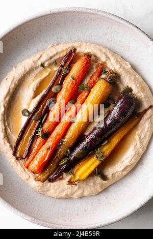 Honiggeröstete Karotten mit Hummus in einer Keramikschale. Stockfoto