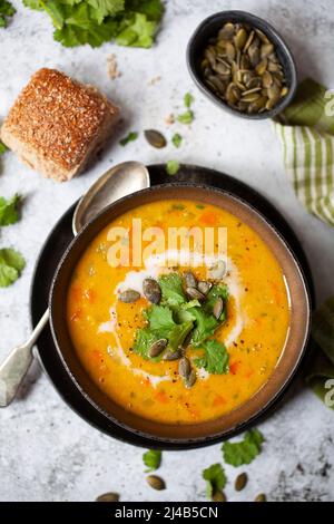 Eine Schüssel mit veganer Karotten- und Koriandersuppe garniert. Mit Kokosmilch, Kürbiskernen und frischem Koriander. Stockfoto