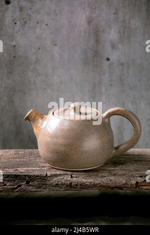 Craft grau rextured handgemachte Keramik Teekocher für Teezeremonie stehen auf alten Holzregal mit grauen Wand im Hintergrund Stockfoto