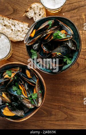 Nahaufnahme einer Schüssel mit Muscheln marinieres mit Petersilie und Bier auf einem Holztisch Stockfoto