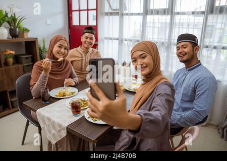 asiatische muslimische Freund machen Selfie zusammen mit Smartphone, während iftar Abendessen Stockfoto