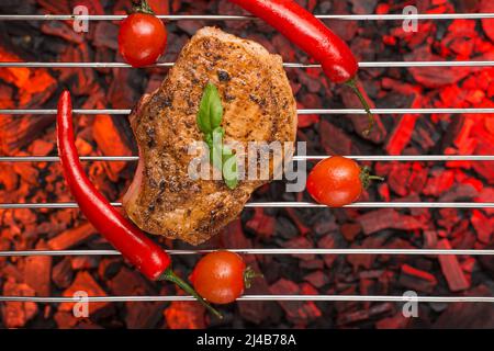 Frisch gegrilltes Steak mit roten Chilischoten, Tomaten und Zwiebelringen. Auf dem Wellpappenrost und auf brennenden Kohlen. Stockfoto