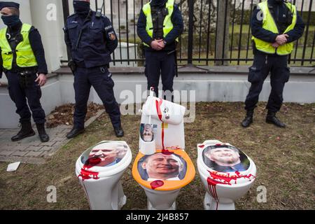 Polizeibeamte stehen als Toilettenschüsseln mit Porträts von: Von links nach rechts werden der weißrussische Präsident Alexander Lukaschenko, der russische Präsident Wladimir Putin und der regionale Führer Tschetscheniens Ramsan Kadyrow während eines anti-russischen Protestes installiert. Vor der russischen Botschaft fand in Warschau ein antirussischer Protest statt, bei dem Warschauer Bürger und Ukrainer absolut jeden Müll, der im Keller zu finden war, zur Botschaft brachten. Der ganze Müll war mit roter Farbe bedeckt, die das Blut der ermordeten ukrainischen Zivilisten symbolisiert. Die Aktion zielte darauf ab, den schändlichen beha zu veröffentlichen Stockfoto