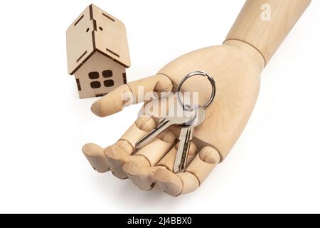 Hölzerne Puppenhand mit Schlüsseln auf der Handfläche mit Spielzeug Holzhaus isoliert auf weiß Stockfoto