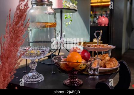 Essen und kalte Getränke werden auf dem Tisch im luxuriösen Hotelzimmer arrangiert Stockfoto