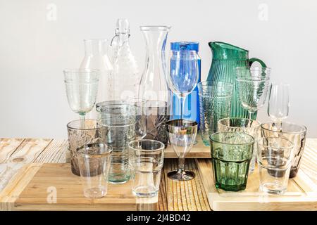 Gläser, Tassen, Flaschen und Gläser in verschiedenen Farben und Texturen auf Bambusplatten und Holztisch Stockfoto