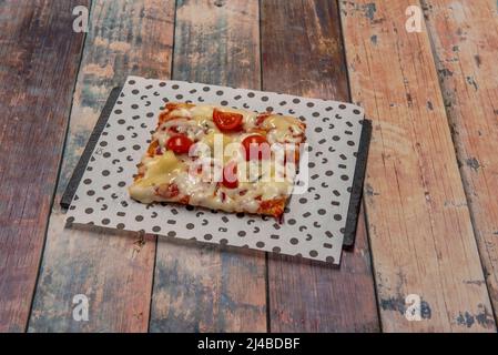 Quadratisches Stück einer frisch gebackenen Pizza mit Gorgonzola-Käse, Kirschtomaten auf einem schwarzen Schieferbrett Stockfoto