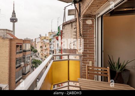 Von einer kleinen Terrasse mit Teakholztisch hat man einen Blick auf einige Gebäude und Terrassen und den Madrider Telekommunikationsturm Stockfoto