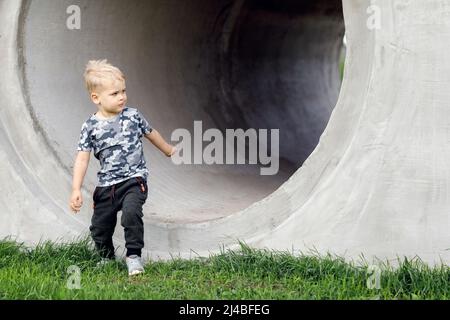 Kleiner Junge, der aus einem grauen Tunnel herauskommt. Tunnelansicht. Ziel erreicht. Rennen von der Dunkelheit zum Licht Stockfoto
