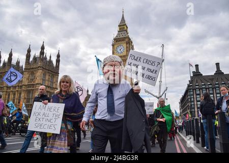 London, Großbritannien. 13. April 2022. Ein Protestler, der eine Boris Johnson Maske trägt, hält ein Plakat mit der Aufschrift „Machtkrise? Wir haben die Macht, ihr habt die Krise" während des Extinction Rebellion Protests auf der Westminster Bridge. Hunderte von Demonstranten marschierten durch das Zentrum Londons und forderten, dass die Regierung gegen die Umwelt- und Klimakrise handelt. Kredit: SOPA Images Limited/Alamy Live Nachrichten Stockfoto