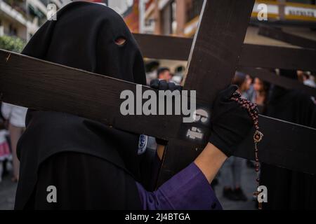 Sevilla, Spanien. 13. April 2022. Ein Christ sah, wie er ein Kreuz auf der Schulter durch die Straßen von Sevilla trug, als sie am Karmittwoch anlässlich der Karwoche an einer Prozession teilnahmen. Die Bruderschaft von San Bernardo nimmt die Prozession von el Cristo de la Salud und la Virgen del Refugio nach zwei Jahren auf die Straße, ohne die Karwoche aufgrund der Einschränkungen der Covid-19-Pandemie zu feiern. Kredit: SOPA Images Limited/Alamy Live Nachrichten Stockfoto