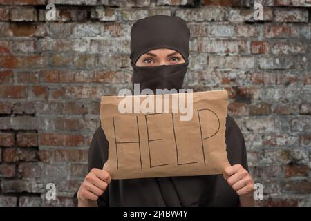 Ein Mädchen aus Syrien trägt einen Hijab in einem Hijab mit einem Litauisch in der Hand und einer Inschrift auf dem Hintergrund von rostrosen Flecken Stockfoto