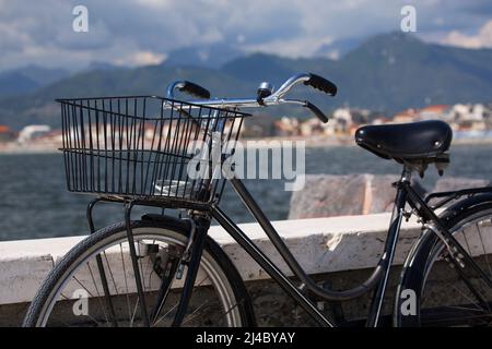 Ein schwarzes Oldtimer-Fahrrad ruht an einem Steindamm am Wasser in Viareggio, in der Toskana in Italien Stockfoto