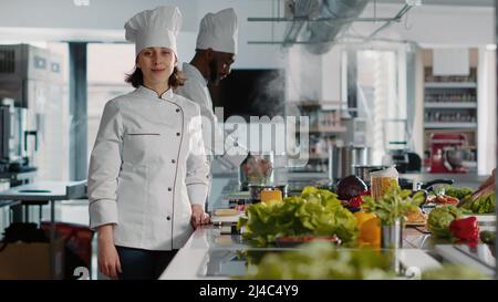 Portrait einer Köchin mit Uniform, die in der Restaurantküche arbeitet und köstliche Gerichte mit kulinarischen Rezepten kocht. Frau, die Gerichte zubereitet, mit frischen Zutaten aus biologischem Anbau. Stockfoto