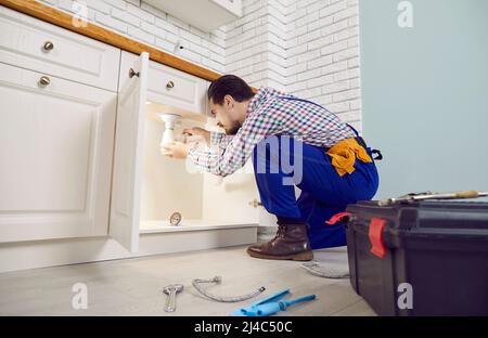 Seriöse professionelle Klempner installiert Siphon unter Waschbecken in der Küche der Wohnung. Stockfoto