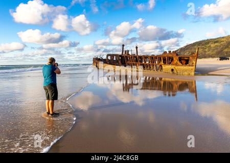 Eine weibliche Touristin fotografiert das berühmte Schiffswrack von Maheno am Eastern Beach auf Fraser Island, Queensland, Australien Stockfoto