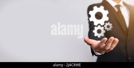 Geschäftsmann im Anzug hält Metallgetriebe und Zahnräder Mechanismus der Interaktion Teamarbeit Konzept, Hand halten Gruppe von virtuellen Zahnräder Rad. Stockfoto