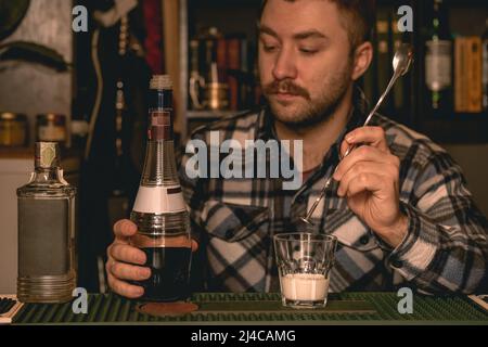 Konzentrierter Barkeeper bereitet alkoholischen Cocktail vor Weißrussisch hinter der Theke Stockfoto