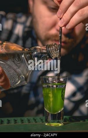 Ein erfahrener Barkeeper bereitet auf der Theke einen Layered Drink Green Mexican zu Stockfoto