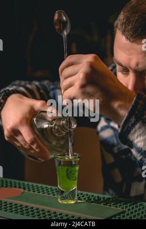 Konzentrierter Barkeeper bereitet traditionellen geschichteten Shot Drink Green Mexican Stockfoto