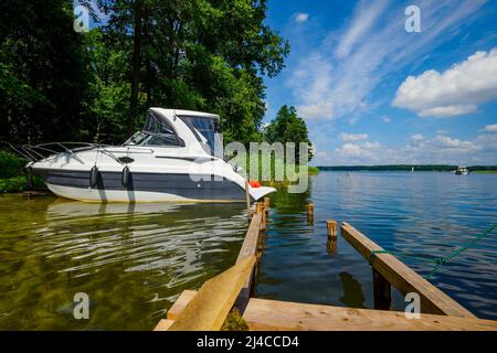 An einem sonnigen Sommertag festgemacht Motorboot in der Nähe eines alten Holzpiers an einem Seeufer Stockfoto