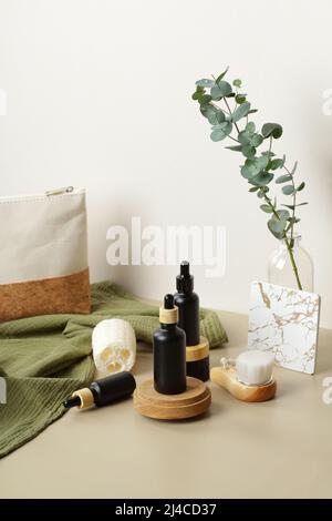 Set aus schwarzen Tropfflaschen und Hautpflegeprodukten auf beigem Tisch mit Kosmetiktasche und Eukalyptus. SPA natürliche Bio-Beauty-Produkte. Stockfoto