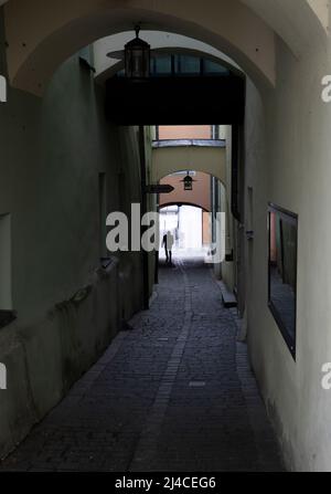 Silhouette eines Mannes, der zwischen Häusern entlang einer engen gepflasterten Straße läuft Stockfoto