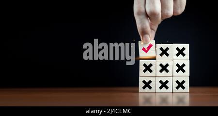 Richtige und falsche Symbol auf Holzwürfel mit Mann Hand wählen richtige Symbol auf dunklem Hintergrund die richtige Idee der Genehmigung, Abstimmung oder Entscheidung. Stockfoto