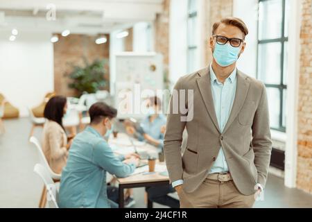 Junger Mann mit Schutzmaske während der Arbeit im Büro Stockfoto