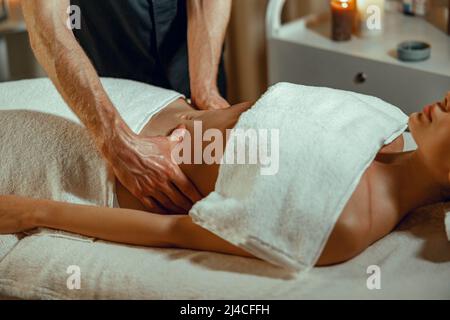 Entspannte junge Frau bekommt professionelle Magenmassage im Spa-Salon Stockfoto