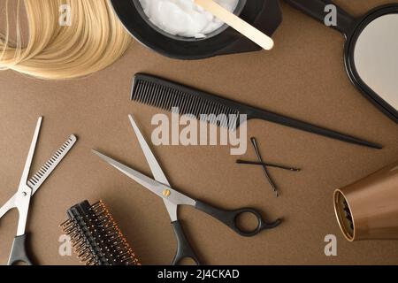 Friseurwerkzeuge zum Schneiden und Färben von Haaren auf braunem Tisch mit Schere, Farbstoff, Pinsel und anderem Arbeitsmaterial. Draufsicht. Horizontale Zusammensetzung. Stockfoto