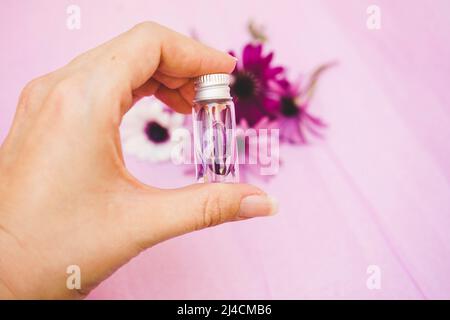 Nahaufnahme einer Hand, die eine Aromatherapie-Flasche mit Wasser und Blütenblättern hält Stockfoto