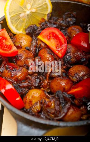 Baby Tintenfisch über rustikalen Holztisch auf eisernen Pfanne mit Tomaten und Zwiebeln gebraten Stockfoto