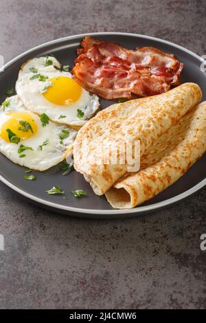 Englisches Frühstück mit Speck, Eiern und Haferflocken Haferpfannkuchen aus der Nähe auf einem Teller auf dem Tisch. Vertikal Stockfoto