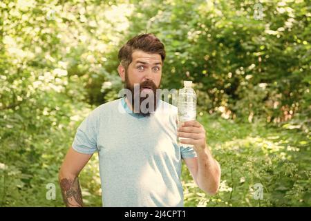 Jogging Trinkwasser. Guy hält den Körper Wasserhaushalt. Hydratation. Täglich Wasser. Erstaunt bärtigen Mann zeigen Flasche. Reife Hipster mit Bart im Wald. Stockfoto