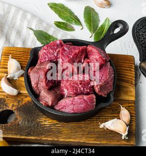 Frisch geschnittenes Rindfleisch, roh, in gusseiserner Pfanne, auf weißer Steinoberfläche, quadratisch Stockfoto