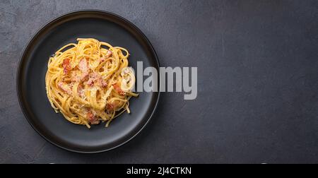 Linguini Pasta mit Carbonara-Sauce auf dunklem Hintergrund. Carbonara-Sauce aus Speck, Parmesan, Eiern, Rahm und Pfeffer. Italienisches Essen. Stockfoto